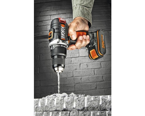 En hand håller en Worx sladdlös borrmaskin som borrar genom en tegelsten.