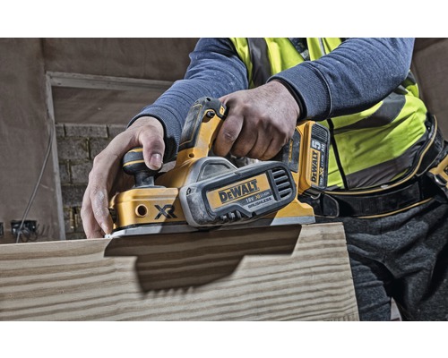 En person hyvlar en träplanka med en elektrisk hyvel. Hyveln är från DeWalt.