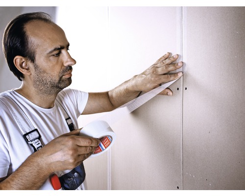 Man fäster glasfibervävtejp på en gipsskivavägg.