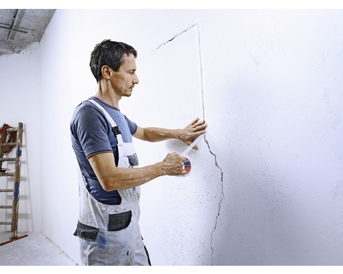 En man tejpar en skadad vägg som förberedelse för reparationer.