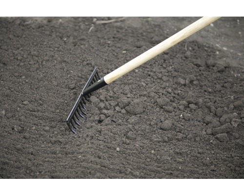 Trädgårdsräfsa med träskaft som används på jorden