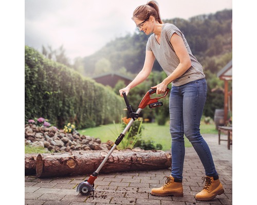 Kvinna använder en kantskärare på en terrass i trädgården.