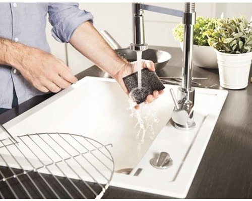 En person rengör en diskho med en svamp under rinnande vatten.