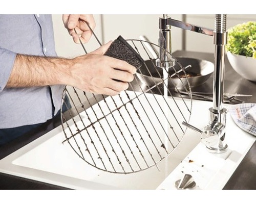 En person rengör ett grillgaller med en svamp ovanför en diskho.
