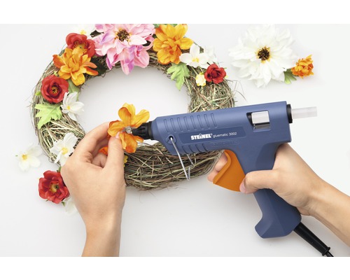 Person som limmar blommor på en krans med limpistol