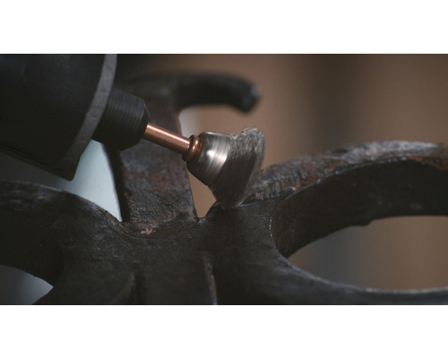 En slipmaskin med stålborstfäste slipar en metallyta.