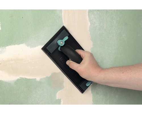 Hand slipar spackel på en vägg med en handslipmaskin