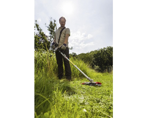 En man arbetar med en grästrimmer i trädgården.