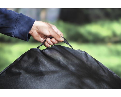 Person håller skyddshuv för trädgårdsmöbler i bärhandtaget