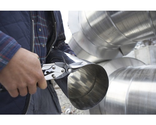 En man skär ett metallrör med plåtsax.