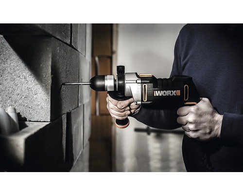 En person borrar i en tegelvägg med en sladdlös borrhammare. Worx logotyp visas.