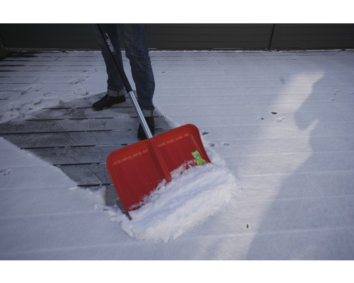 Person som skottar snö med en snöskyffel från en träterrass