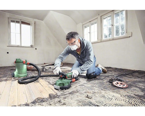 En man slipar ett trägolv med en betongslipmaskin i ett ljust rum.