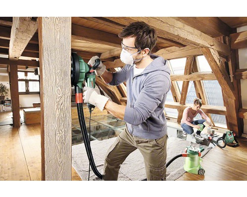 Man slipar en träbjälke med en väggslipmaskin på en vind.