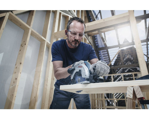 En man sågar en bräda med en cirkelsåg i ett råbygge