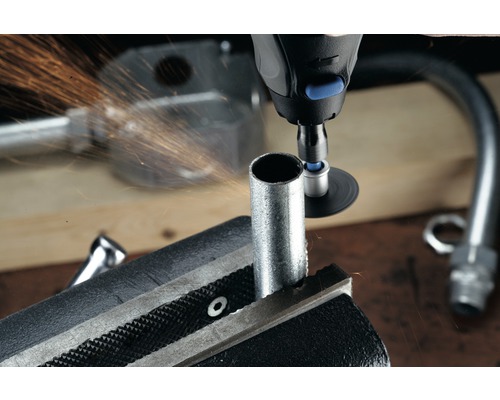 En rörtång håller ett rör medan ett multifunktionsverktyg bearbetar det och gnistor sprutar.