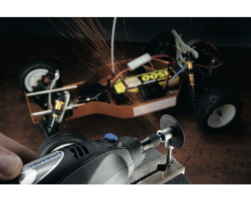 Dremel logotyp. En person bearbetar ett arbetsstycke med ett Dremel multiverktyg, gnistor flyger. En modellbil syns i bakgrunden.