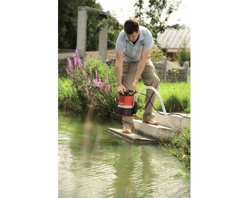 Man som använder en smutsvattenpump på stranden av ett vattendrag.
