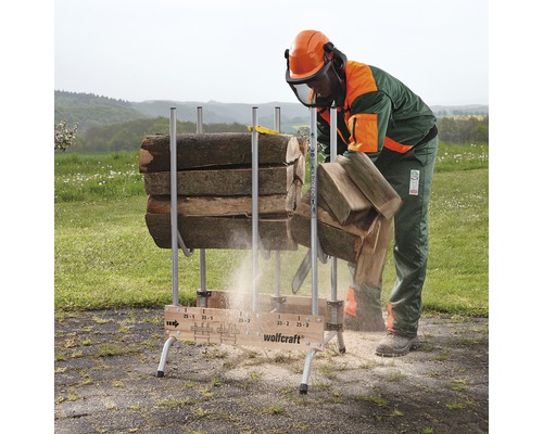 En person med skyddskläder sågar trä med en motorsåg på en vedbock från Wolfcraft