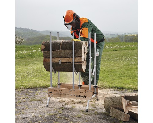 En person med skyddsutrustning sågar ved på en Wolfcraft sågbock.