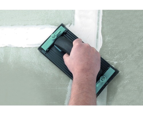 En hand använder en slipbräda för att jämna ut en spacklad vägg.