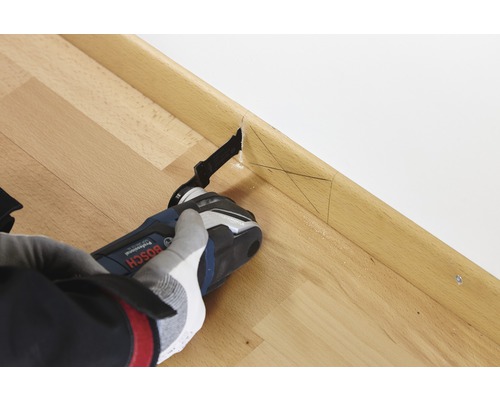 En person använder en multifunktionsskärare på en golvlist av trä för att göra ett exakt snitt.