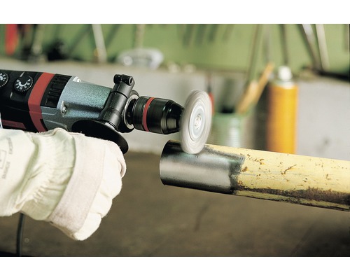 En person använder en borr med en stålborste på ett rör för att ta bort rost.