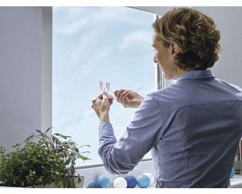 Kvinna fäster självhäftande remsor på fönstret för att fästa fönsterdekorationer