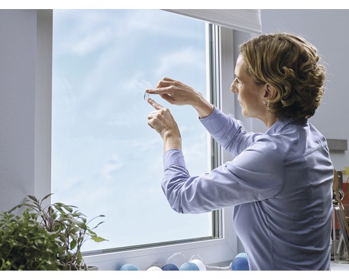 Kvinna fäster fönsterfilm på en fönsterruta för dekoration och avskildhet