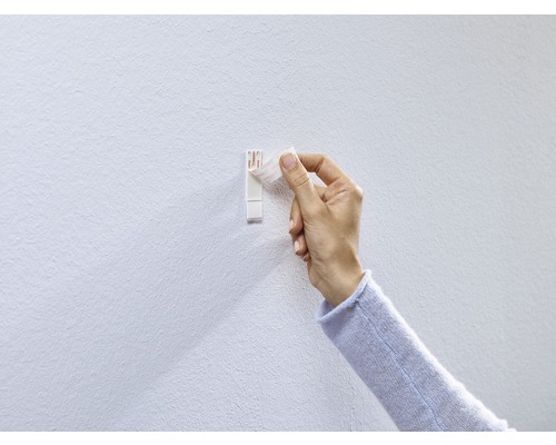 Person som fäster en självhäftande krok på väggen