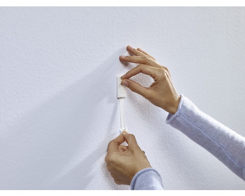 En person fäster en självhäftande remsa på en vägg.