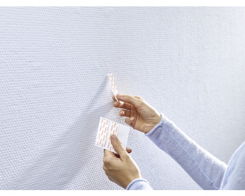 Händer fäster en självhäftande remsa på en vägg