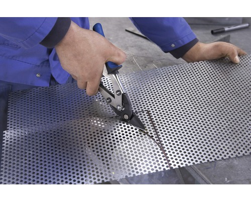 En person skär en perforerad plåt med plåtsax.