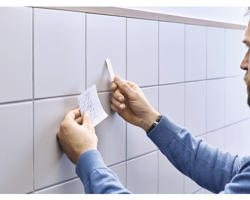Man fäster självhäftande remsor på kakel för väggmontering