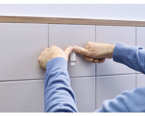 Man fäster en självhäftande krok på en kakelvägg.