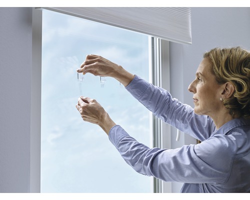Kvinna fäster självhäftande krokar på fönstret för montering av solskydd