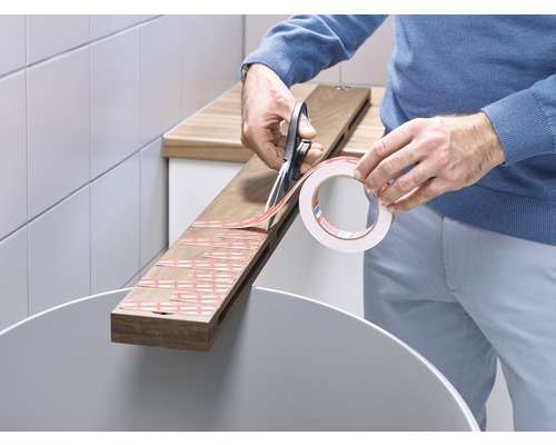 En person klipper dubbelhäftande tejp med en sax på en träbräda.