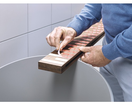 En person tar bort skyddsfilmen från dubbelsidiga tejpbitar på en trälist för montering.