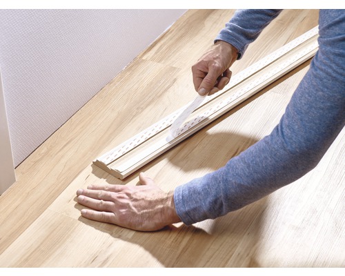 En person fäster en golvlist på en vägg med dubbelsidig tejp.