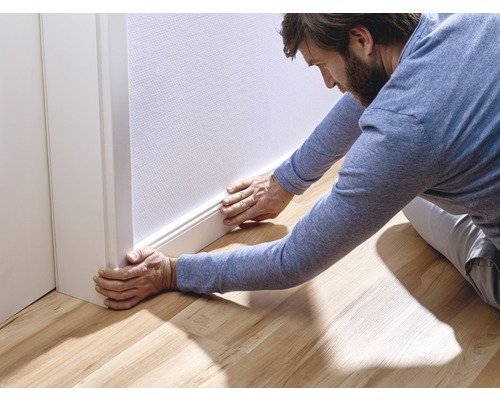 Man installerar en golvsockel mot en vägg på ett trägolv.