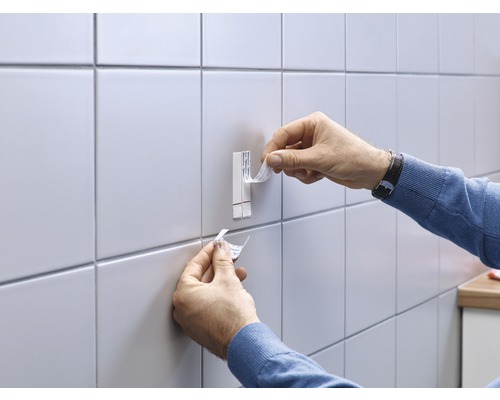 Person fäster en självhäftande krok på en kakelvägg