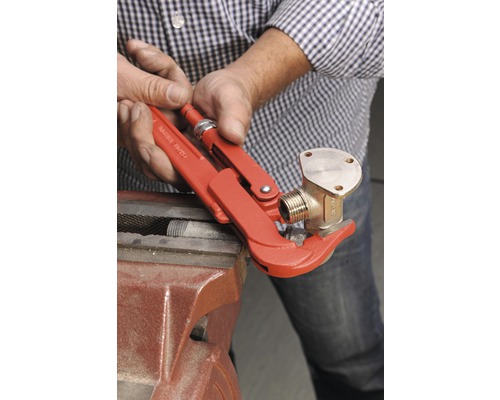 En person fäster en mässingskoppling med en rörtång i ett skruvstäd.