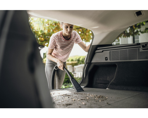 Kvinna dammsuger bagageutrymmet på en bil med en dammsugare