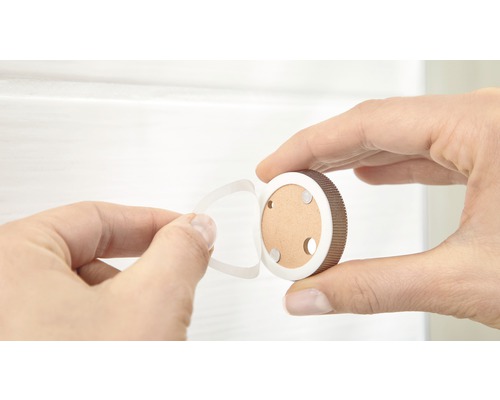 En hand håller ett runt magnetlåsfäste och tar bort skyddsfilmen från den självhäftande dynan.