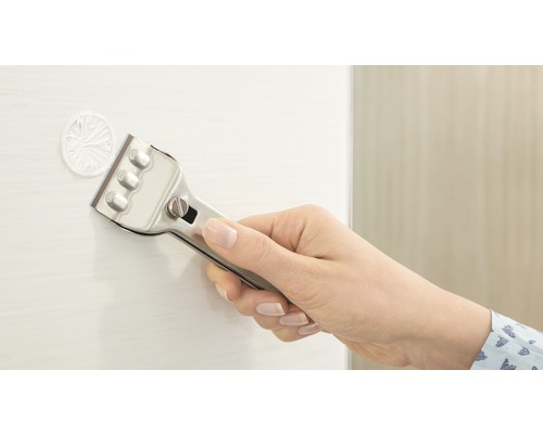 Hand med glasskrapa tar bort klistermärke från en yta