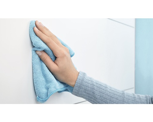 En hand torkar av en vit yta med en mikrofiberduk