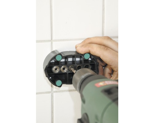 En borrmaskin borrar genom en borrmall i en kakelvägg.