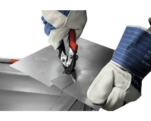 En hand med skyddshandske klipper en plåt med en plåtsax.