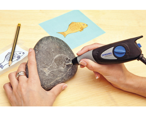 En person graverar ett fiskmönster i en sten med ett Dremel graveringsverktyg.