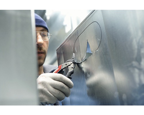 En man klipper ett hål i en plåt med en plåtsax.